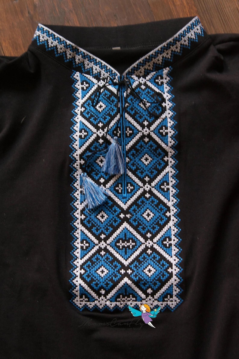May include: Black shirt with intricate blue and white embroidered geometric patterns. The design features diamond and cross motifs, with a detailed collar and tassel ties. A small illustration is visible at the bottom right.