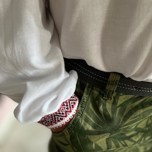 May include: Close-up of a pocket with a red, white, and black patterned design. The pocket is part of green camouflage pants. A white shirt is visible above the pocket.