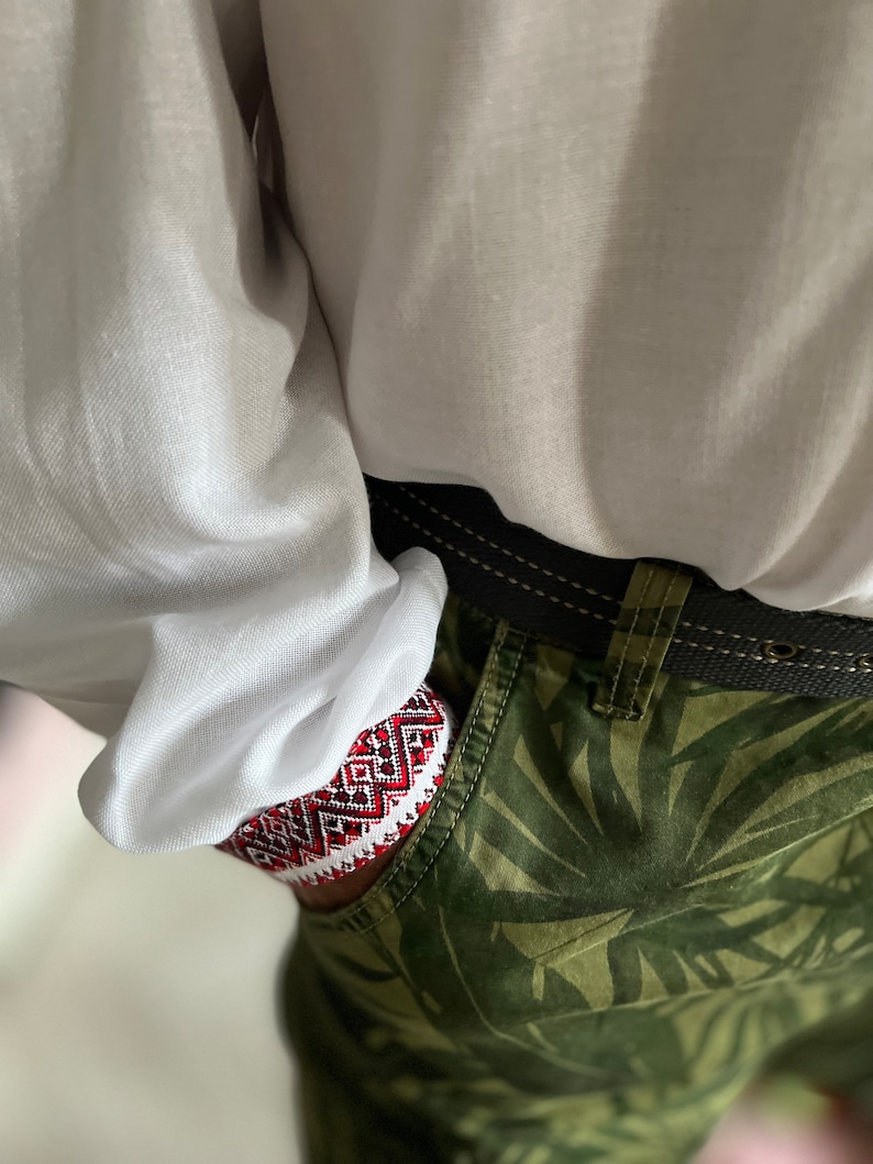 May include: Close-up of a pocket with a red, white, and black patterned design. The pocket is part of green camouflage pants. A white shirt is visible above the pocket.