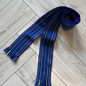 Op de afbeelding: Een geweven riem in blauw en wit met franjes aan de uiteinden.