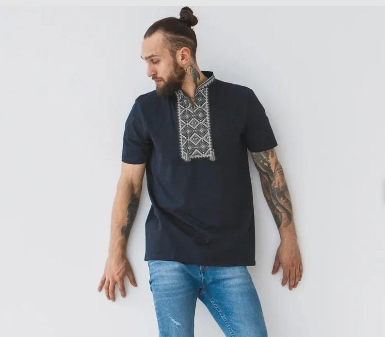 May include: A navy blue short-sleeved shirt with an embroidered geometric design on the collar. The shirt is paired with light blue denim jeans. The shirt's design features white and gray patterns.
