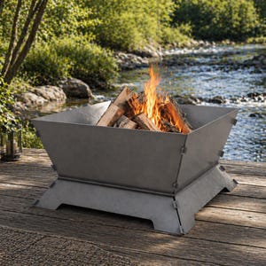 May include: A square, gray metal fire pit with a wood fire burning inside. The fire pit is on a wooden deck near a river. The flames are orange and yellow, and the wood is brown. The fire pit is empty.