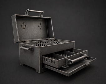 Puede incluir: Una pequeña parrilla de metal desgastado con tapa abierta y cajón extraíble. La parrilla tiene un asa en la parte superior y otra en el cajón. La parrilla es de color gris oscuro y se encuentra sobre un fondo oscuro.