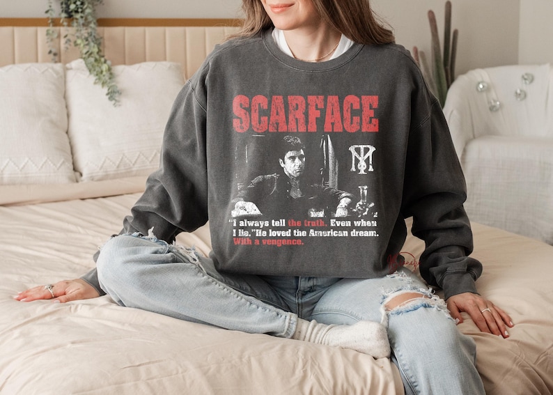 K&ouml;nnte beinhalten: Dunkelgraues Sweatshirt mit dem Wort "SCARFACE" in Rot und einem Schwarz-Wei&szlig;-Bild eines Mannes. Das Sweatshirt enth&auml;lt auch das Zitat: "Ich sage immer die Wahrheit. Auch wenn ich l&uuml;ge. Er liebte den amerikanischen Traum. Mit Rache."
