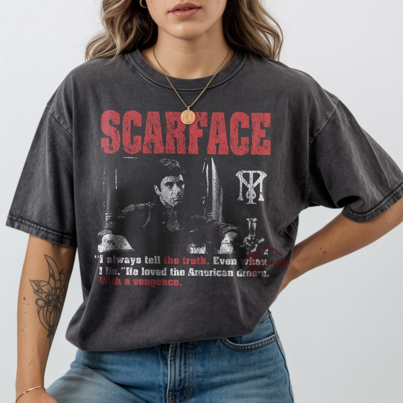 K&ouml;nnte beinhalten: Dunkelgraues T-Shirt mit dem Wort "SCARFACE" in roten Blockbuchstaben. Darunter ein Schwarz-Wei&szlig;-Bild eines Mannes, ein Zitat und ein Logo. Das T-Shirt wird von einer Person getragen. Das Shirt ist aus weichem Material.