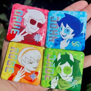以下が含まれることがあります： アニメスタイルのキャラクターが描かれた4つの正方形のピンバッジ。ピンクのバッジにはDAVE、青いバッジにはJOHN、黄色いバッジにはROSE、緑のバッジにはJADEという文字がそれぞれホログラム加工で記されています。