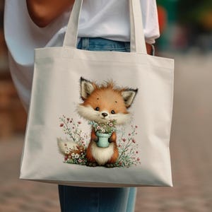 May include: A cream-colored tote bag featuring a charming illustration of a cartoon fox holding a small blue pot filled with flowers. The fox has orange fur, a white chest, and is surrounded by delicate floral accents. The bag is carried by a person.