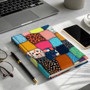 May include: A colorful patchwork journal with a variety of patterns and colors, including blue, pink, yellow, and orange. A laptop, smartphone, pen, glasses, and a cup of coffee are also on the desk.