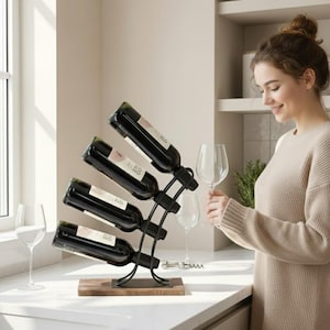 May include: A black metal wine rack with a rectangular wooden base, designed to hold four wine bottles at an upward angle. The rack features a curved frame that supports the bottles in a stacked, diagonal arrangement on a flat surface.