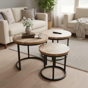 May include: A set of three round nesting tables with natural wood tops featuring white geometric zigzag patterns and black metal frames. The tables are arranged in a tiered formation, with the largest table holding a vase of white flowers.