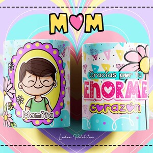 Puede incluir: Dos tazas de cer&aacute;mica blanca con dise&ntilde;os coloridos. Una taza presenta una ilustraci&oacute;n de dibujos animados de una persona con gafas y el texto "Mamita". La otra taza tiene un dise&ntilde;o colorido con el texto "Gracias por tu enorme coraz&oacute;n".