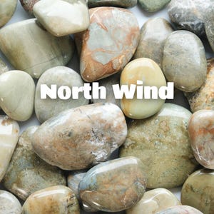 May include: An assortment of polished stones in different shapes and sizes. The stones are in shades of beige, tan, and touches of green and orange. The image includes the text "North Wind".