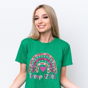 A smiling woman wearing a green t-shirt with a rainbow graphic and text.