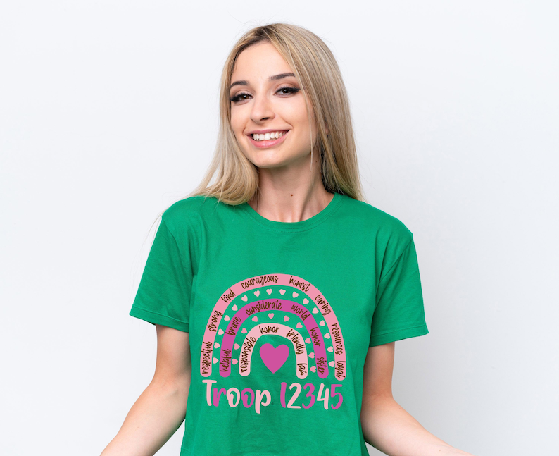 A smiling woman wearing a green t-shirt with a rainbow graphic and text.