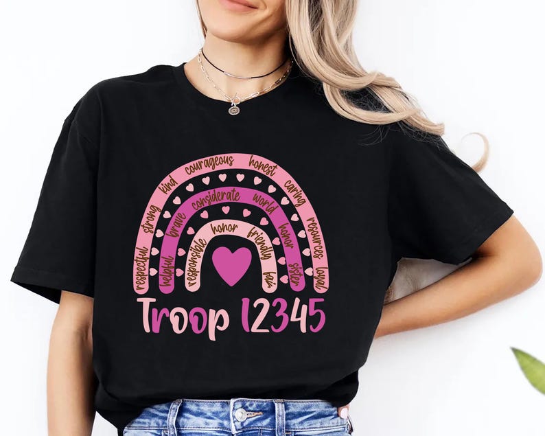 A woman wearing a black t-shirt with a graphic design featuring a rainbow and the words "Troop 12345" printed on it. girl socut camping troop