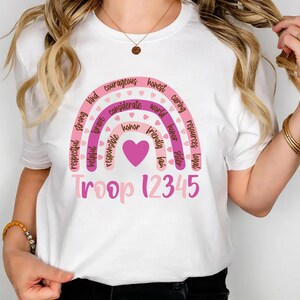 A woman wearing a white t-shirt with a colorful graphic design and text printed on it.