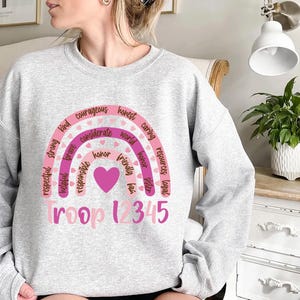 a woman sitting on a bed wearing a sweatshirt with a rainbow