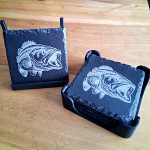 May include: Set of four black slate coasters with a white engraved image of a bass fish. The coasters are in a black holder.