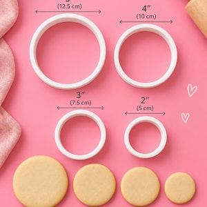 Könnte beinhalten: Vier weiße, kreisförmige Ausstechformen in den Größen 12,5 cm, 10 cm, 7,5 cm und 5 cm, begleitet von vier passenden runden Keksen. Der Text 4 SIZES und Perfect for cookies, fondant, clay and more! ist auf dem rosa Hintergrund gedruckt.
