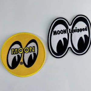 May include: Two embroidered patches. One is a circular yellow patch featuring the black and white Moon eyes logo with the text MOON. The second is a white patch shaped like two connected eyes with black outlines and the text MOON Equipped.