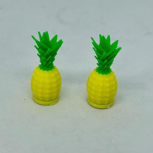 Op de afbeelding: Twee kleine gele ananasvormige figuurtjes met groene toppen.
