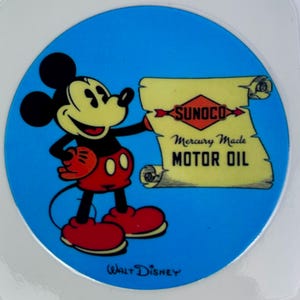 May include: A circular blue sticker featuring Mickey Mouse with a scroll. The scroll reads "SUNOCO Mercury Made MOTOR OIL." Mickey is in red shorts, shoes, and gloves. The words "Walt Disney" are at the bottom.