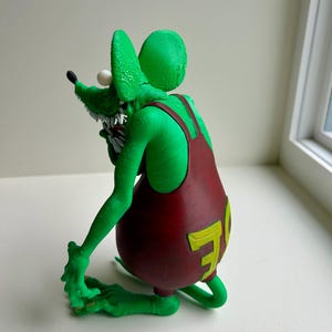 Peut inclure: Figurine de rat vert &agrave; l'expression mena&ccedil;ante, portant une salopette bordeaux avec un "70" jaune au dos. Le rat a des dents pointues, un &oelig;il blanc et un nez noir. La figurine est pos&eacute;e de mani&egrave;re dynamique.