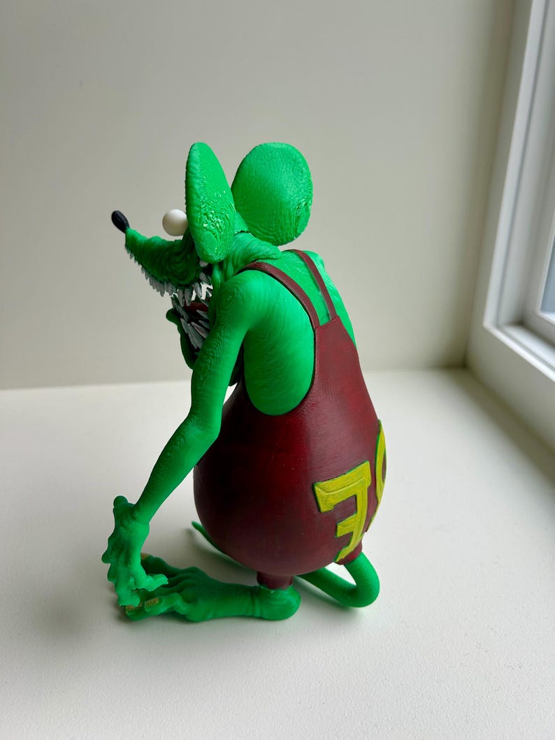 Peut inclure: Figurine de rat vert &agrave; l'expression mena&ccedil;ante, portant une salopette bordeaux avec un "70" jaune au dos. Le rat a des dents pointues, un &oelig;il blanc et un nez noir. La figurine est pos&eacute;e de mani&egrave;re dynamique.