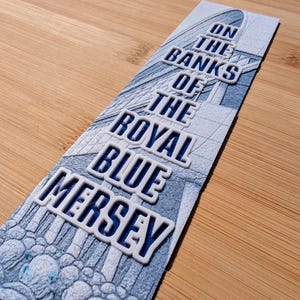 May include: A blue and white bookmark with the text "On the Banks of the Royal Blue Mersey".