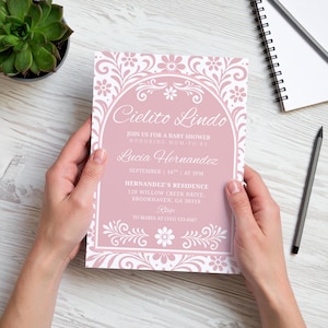May include: A pink baby shower invitation with white floral and scroll design. The invitation includes the text "Cielito Lindo" and details for Lucia Hernandez's baby shower, including the date, time, and location.