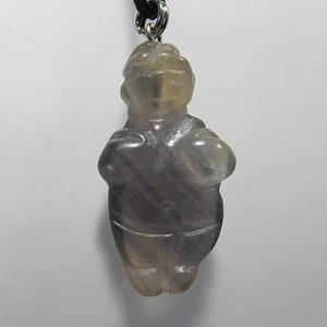 May include: A gray carved stone figurine pendant, shaped like a person, with a silver bail.