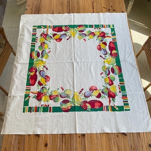 May include: White tablecloth with a colorful border featuring a repeating pattern of fruits and vegetables in red, yellow, and green. The border is a green rectangle with colorful stripes.