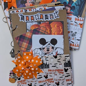 May include: A handmade Halloween-themed scrapbook with Mickey Mouse illustrations. The scrapbook features orange and white polka dot bows, decorative paper, and the words "Halloween Time." The pages include pumpkin and bat designs.
