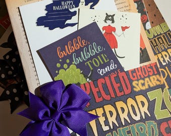 May include: A collection of Halloween-themed cards and ephemera, including cards with text that reads "Happy Halloween" and "bubble, bubble, toil and". A purple bow adorns the front. The background includes book pages and patterned paper.