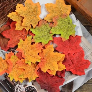 May include: A collection of artificial fall leaves in various shades of red, orange, yellow, and green. The leaves are made of a fabric-like material and have a realistic appearance.