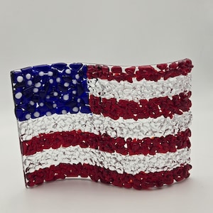 May include: A glass American flag made with red, white, and blue glass pieces. The flag is waving in the wind.