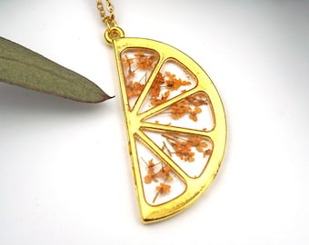 May include: Gold necklace with a pendant shaped like a slice of lemon with dried orange flowers inside.