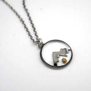 May include: A silver chain necklace with a round pendant. The pendant is clear and has a silver mountain design inside. A small gold bead is also inside the pendant.