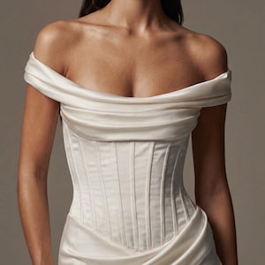 May include: Ivory satin corset top with an off-the-shoulder design. The bodice features vertical paneling, and the fabric drapes elegantly. This formal top is suitable for special occasions.