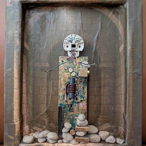 May include: Mixed media artwork featuring a robot-like figure constructed from electronic components. The figure stands within a framed, textured background depicting an ancient architectural setting. The artwork incorporates stones at the base and has a gold-painted frame.