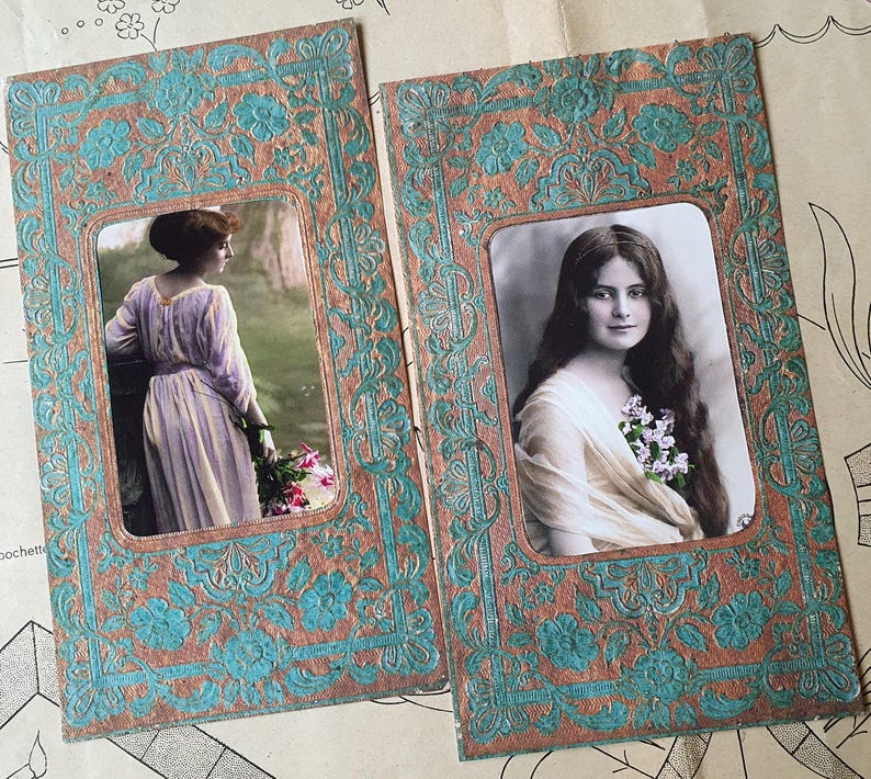 Op de afbeelding: Twee vintage ansichtkaarten met sierlijke lijsten met afbeeldingen van vrouwen. De lijsten zijn versierd met een turquoise en bruin bloemenpatroon. De vrouwen zijn gekleed in vintage kleding en hebben lang haar.