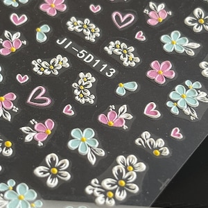 May include: A sheet of nail art stickers featuring a variety of floral designs in white, pink and blue. The stickers include small flowers, hearts and leaves. The sheet is labelled "JI-5D113".