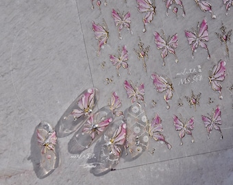 May include: Clear nail art stickers featuring pink and gold butterflies and decorative accents. The stickers are arranged on a clear sheet, with some applied to acrylic nails. The text "merle" and "MS 561" is visible.