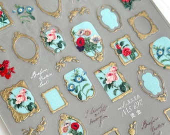 May include: A sheet of nail art stickers featuring various designs. The stickers include gold-colored frames, light blue backgrounds, and floral arrangements in shades of red, pink, and white. Some stickers have script text.