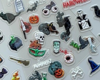 May include: Sheet of Halloween-themed stickers with various designs. Includes pumpkins, ghosts, bats, witch hats, tombstones, and the text "Happy Halloween." The stickers are in shades of orange, black, white, and green.