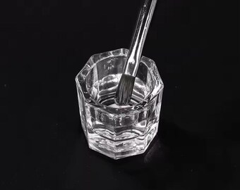 May include: A clear glass dish with a textured surface, filled with a clear liquid. A silver brush is partially submerged in the liquid.