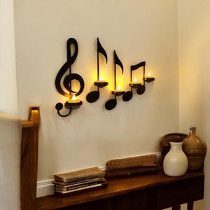 May include: Black metal wall decor featuring a treble clef and musical notes with candle holders. The candle holders are lit with warm yellow flames.