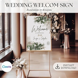 Könnte beinhalten: Ein rechteckiges Hochzeits-Willkommensschild auf einem goldfarbenen Metallständer mit grünen Eukalyptusblatt-Illustrationen, schwarzem Schriftzug Welcome to our wedding sowie den Namen Jennifer & Stephen und dem Datum 22 2024 auf weißem Grund.