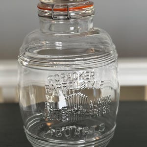 Puede incluir: Tarro de cristal transparente con tapa abisagrada y junta de goma naranja. El tarro está grabado con "Cracker Barrel Style", "Full Value" y "Always Fresh". Tiene una capacidad de 3,79 litros.