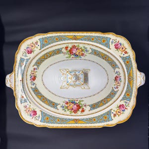 以下が含まれることがあります： 蓋付きの白い磁器製のサービングディッシュ。ディッシュには、ピンク、イエロー、ブルーの花のフラワーパターンが施されています。蓋には金色のノブが付いています。